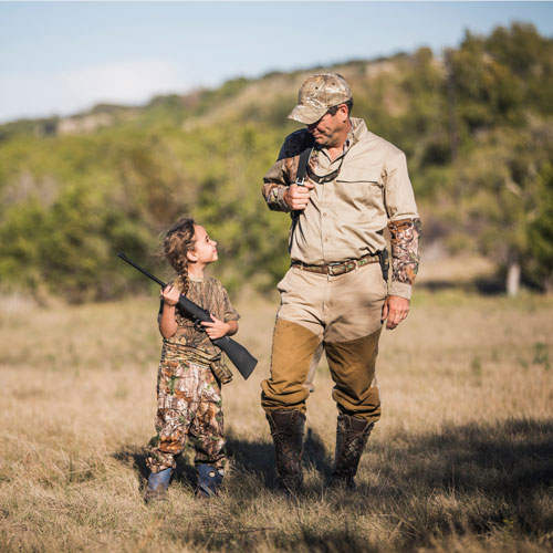 Girl-holding-rifle-while-looking-at-father-in-field
